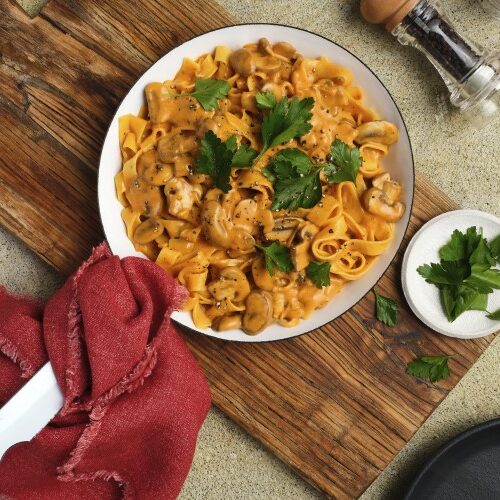 A skillet, ready to serve, filled with Gluten-Free Mushroom Stroganoff with plates and utensils next to it.