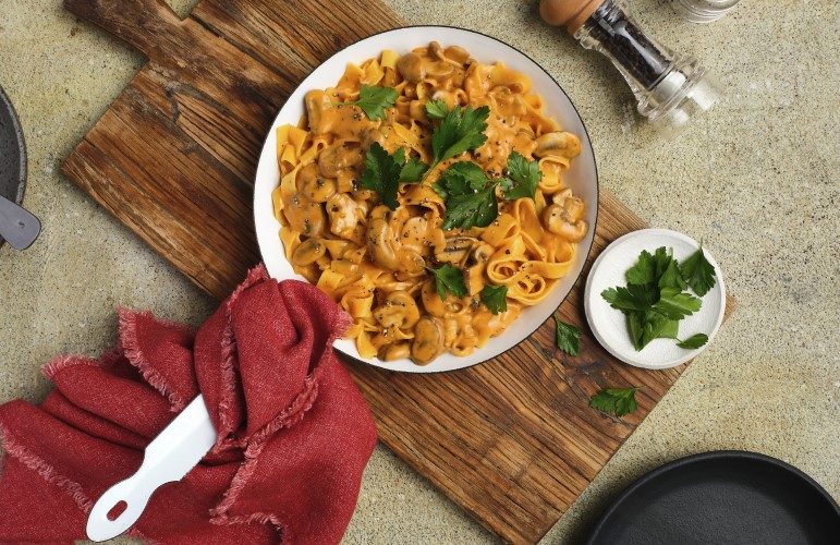 A skillet, ready to serve, filled with Gluten-Free Mushroom Stroganoff with plates and utensils next to it.