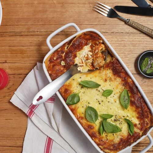 A bake dish with Mostaccioli Lasagne with a filled serving spoon ready to serve.