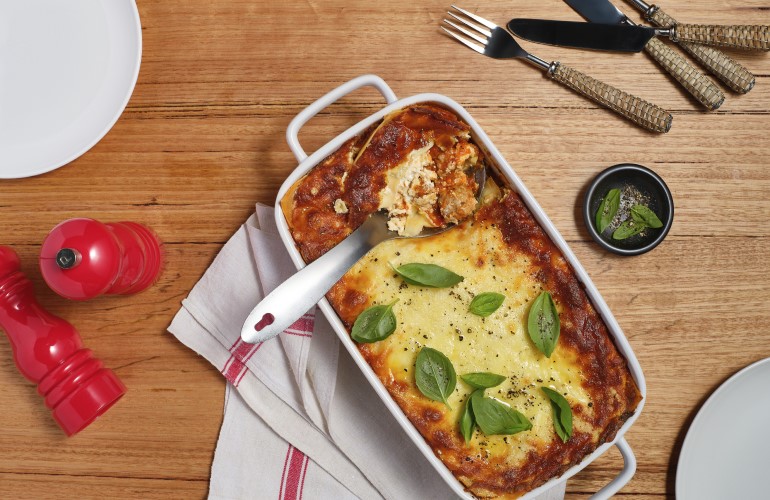 A bake dish with Mostaccioli Lasagne with a filled serving spoon ready to serve.